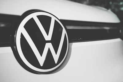 A close-up of a Volkswagen logo centered on the front of a vehicle, displaying the iconic VW letters in a bold, black and white design against a smooth, clean surface.