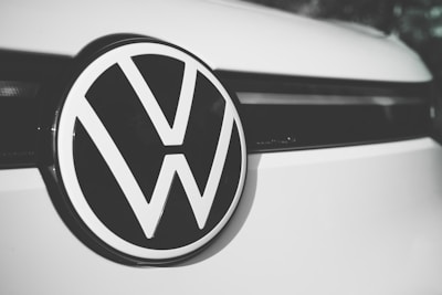 A close-up of a Volkswagen logo centered on the front of a vehicle, displaying the iconic VW letters in a bold, black and white design against a smooth, clean surface.