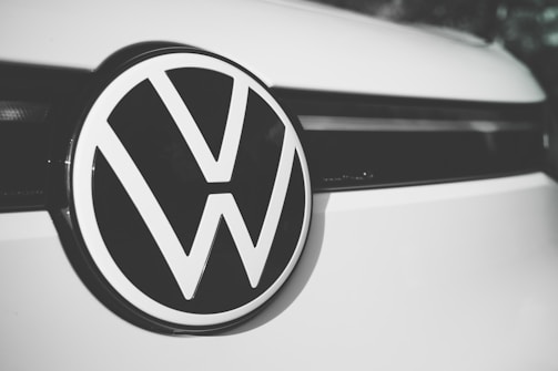 A close-up of a Volkswagen logo centered on the front of a vehicle, displaying the iconic VW letters in a bold, black and white design against a smooth, clean surface.