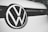 A close-up of a Volkswagen logo centered on the front of a vehicle, displaying the iconic VW letters in a bold, black and white design against a smooth, clean surface.