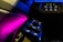 A car's interior control panel is illuminated with vivid colors, featuring buttons and switches for various functionalities like front and rear control, temperature settings, and automatic mode. The lighting creates a striking contrast against the dark dashboard.