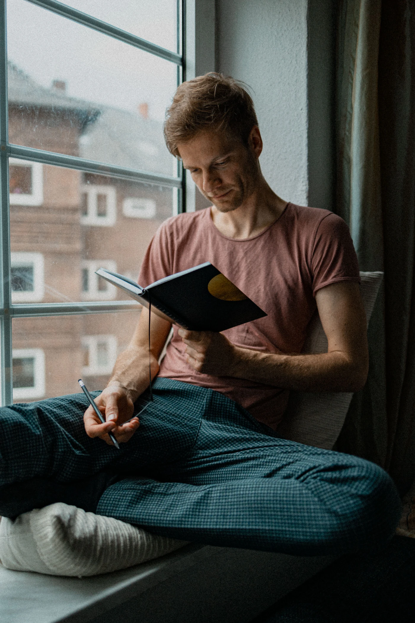Man reading a notebook in a chair by a window