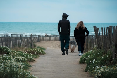 man and woman walking on brown wooden dock near body of water during daytime