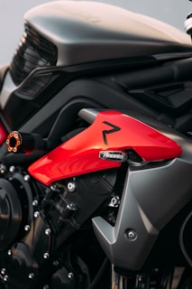A close-up view of a motorcycle's side, highlighting its red and black body. The image features sleek, modern design elements with visible bolts and a glossy finish. The red panel is particularly striking against the dark metal components.