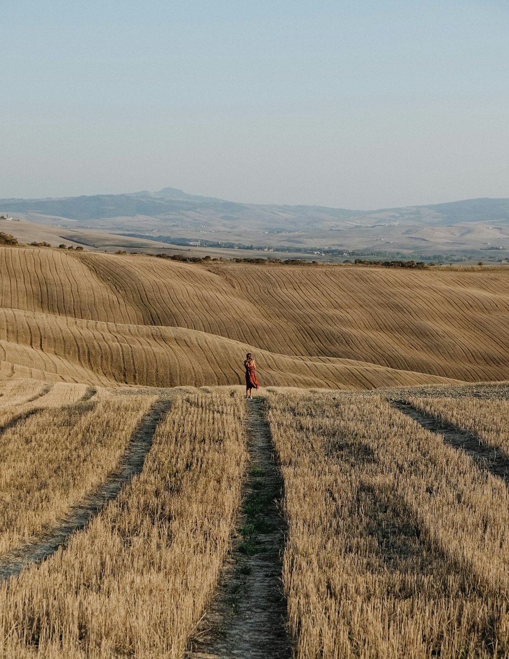 Persona in giacca rossa che cammina sul campo marrone durante il giorno