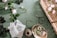 A collection of gardening items and flowers laid out on a green surface. There are various plants and roses scattered around, some in a wicker basket. Seed packets depicting different kinds of flowers, a ball of twine, and gardening shears are also visible. The scene is organized yet has a sense of natural flow.