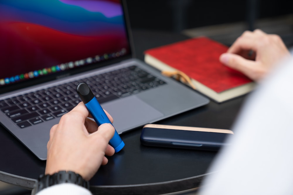 person holding blue pen near macbook pro