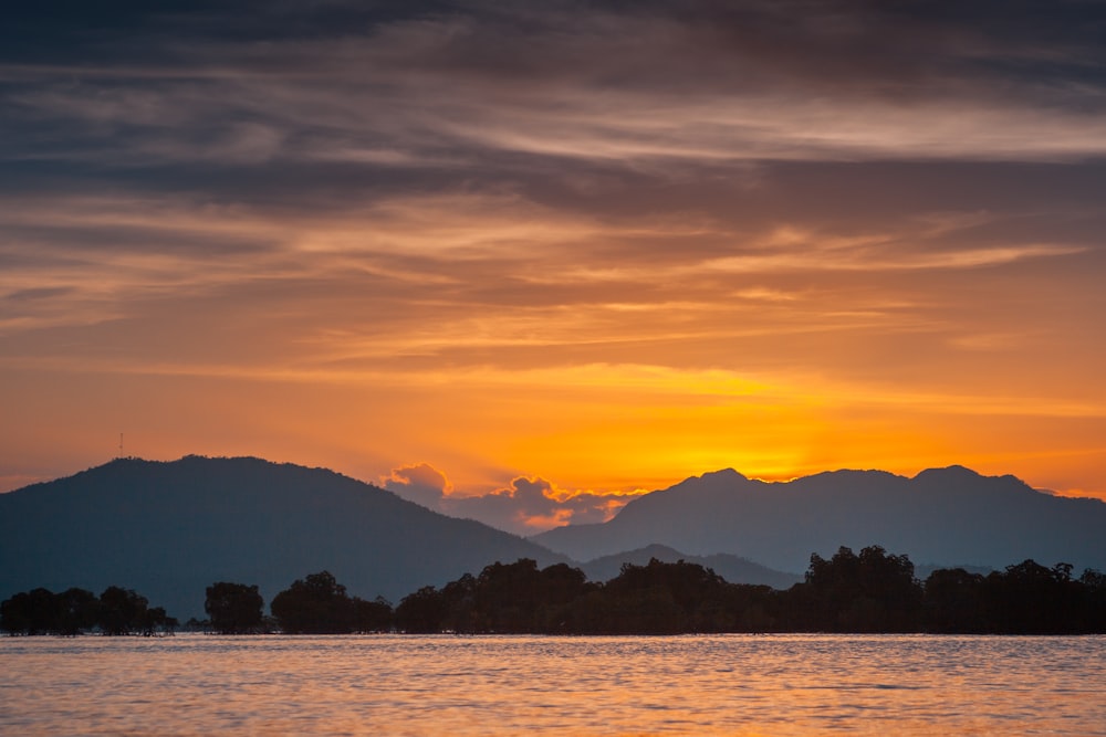 silhouette of mountain near body of water during sunset