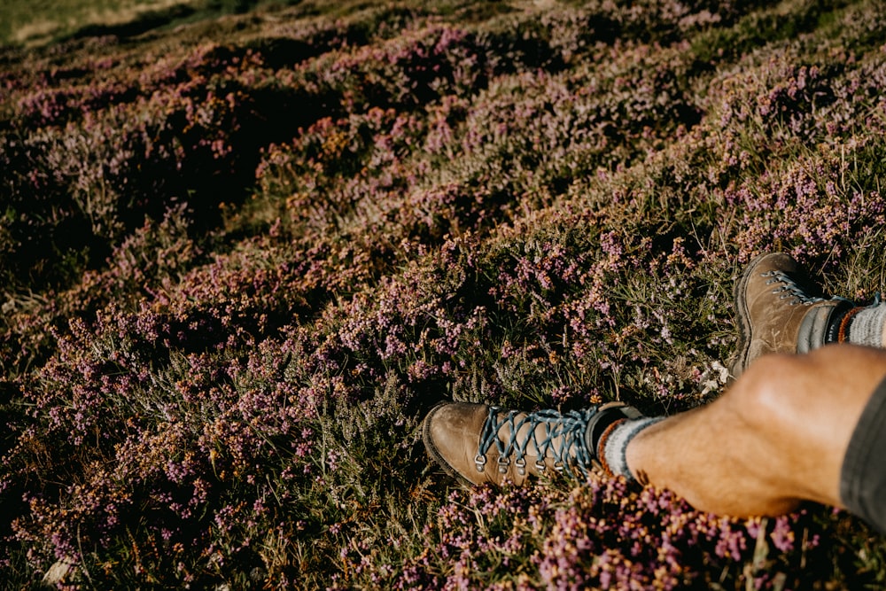 personne portant des chaussures à lacets marron et blanc debout sur un champ d’herbe verte pendant la journée