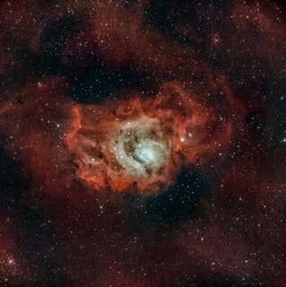 A vast cosmic scene featuring a bright nebula with a glowing core surrounded by swirling red and orange clouds. Countless stars are scattered throughout the dark expanse, adding to the depth and complexity of the scene.