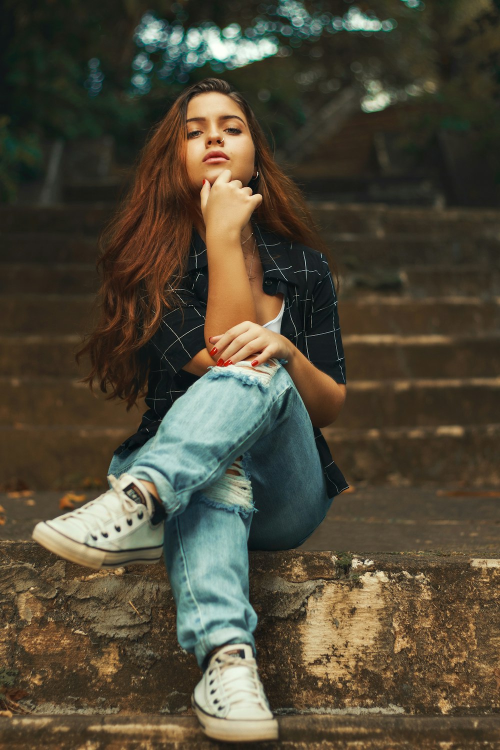 woman in blue denim jeans and white converse all star high top sneakers sitting on brown