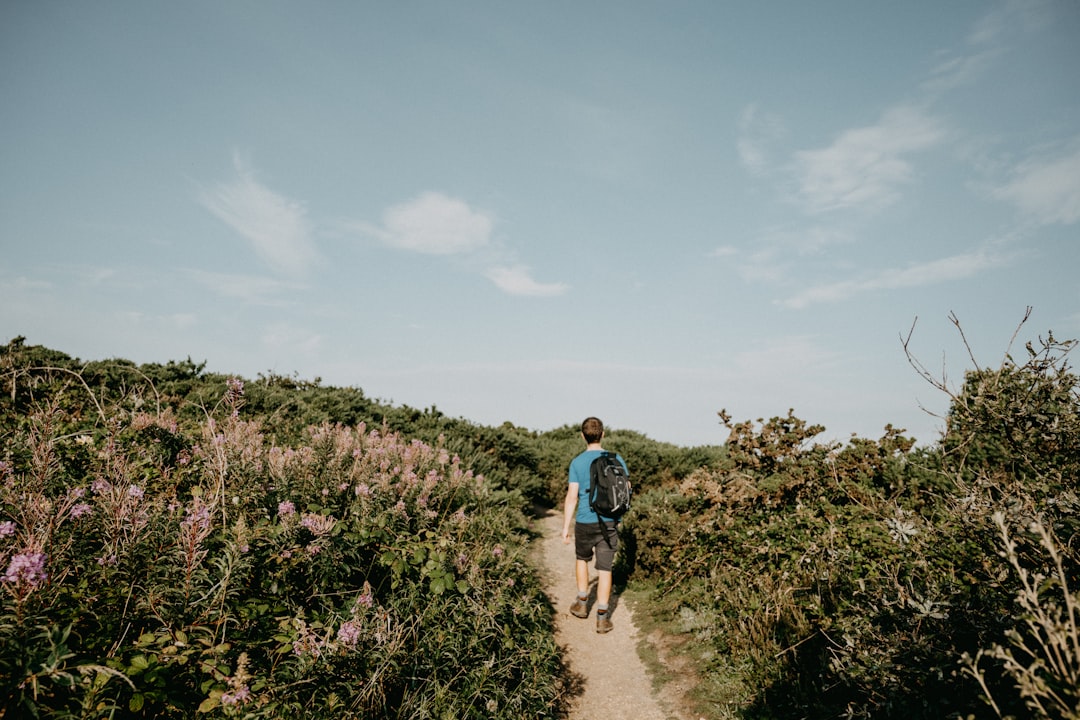 man in black t-shirt and black shorts walking on pathway between green plants during daytime