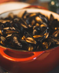 A close-up shot of freshly cooked mussels with vibrant yellow flames in the background, highlighting the fiery cooking process.