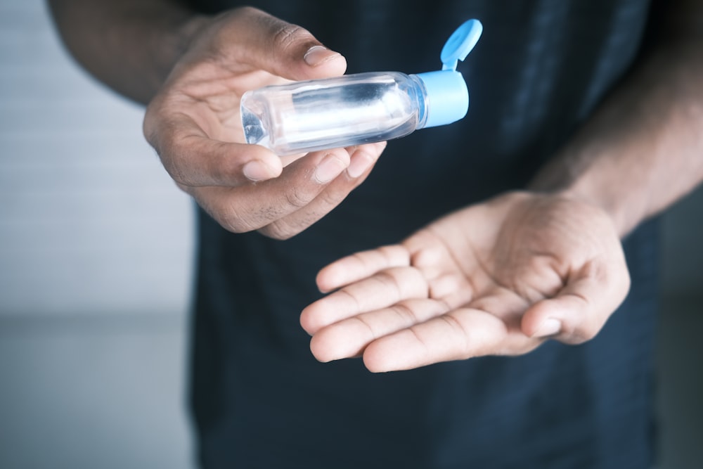 Persona sosteniendo una botella de vidrio transparente con tapa azul