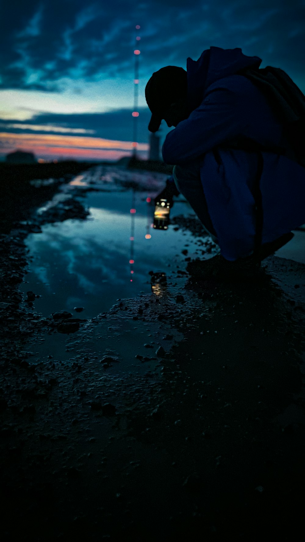 person in blue hoodie and black pants standing on wet ground during sunset