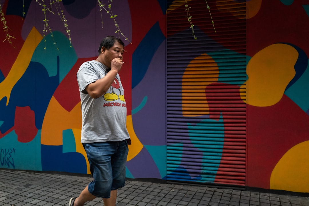 boy in white t-shirt and blue pants standing near wall with graffiti during daytime