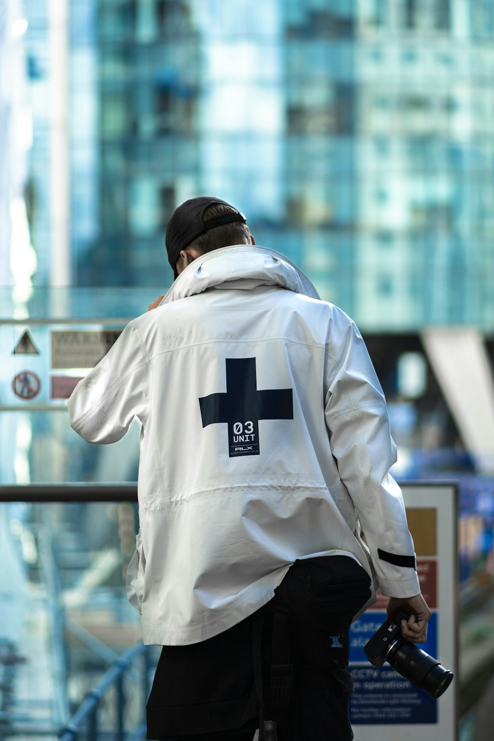 homem em branco e preto adidas hoodie de pé perto de grades de metal azul durante o dia