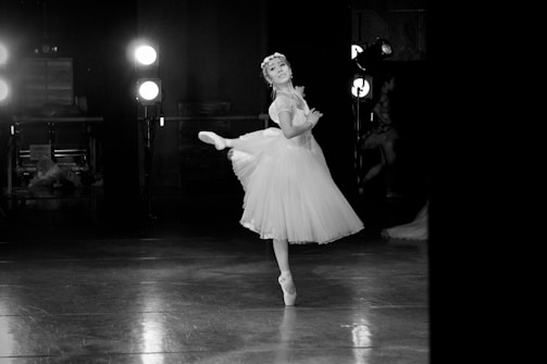 A ballerina gracefully performs en pointe in a dimly lit studio, her tutu softly lit by spotlights. She embodies elegance and concentration, surrounded by an ambiance of classic dance.