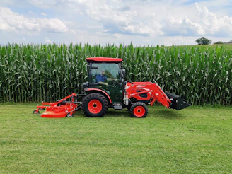 red tractor on green grass field under white clouds during daytime