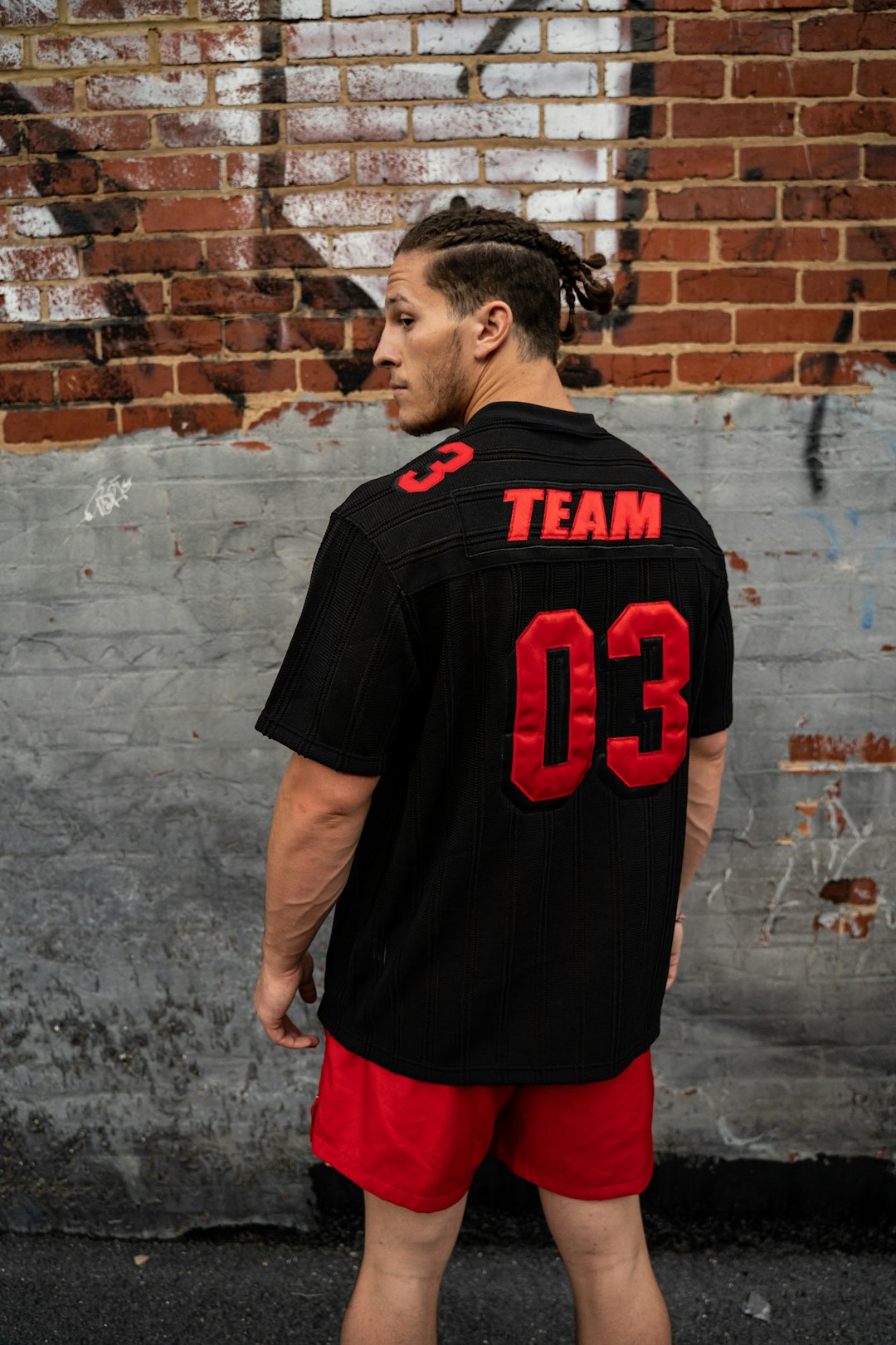 man in black and red crew neck t-shirt standing near brown brick wall