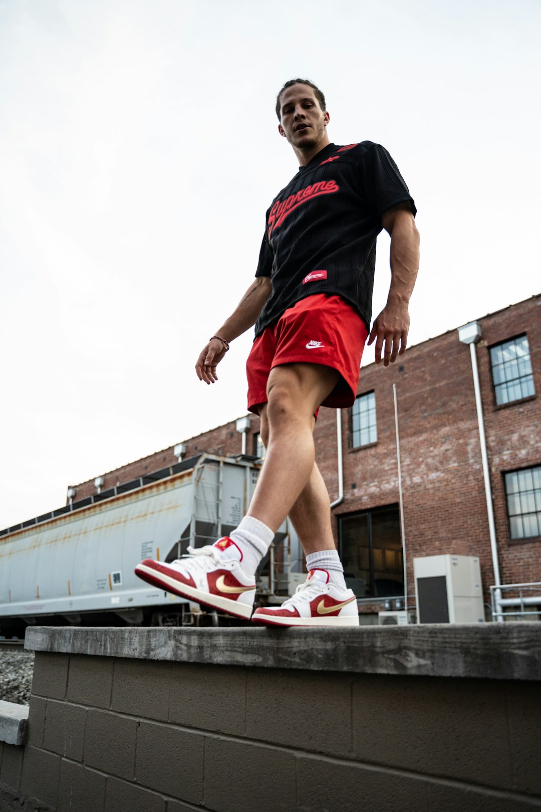 man in black and red nike t-shirt and red shorts jumping on gray concrete bridge