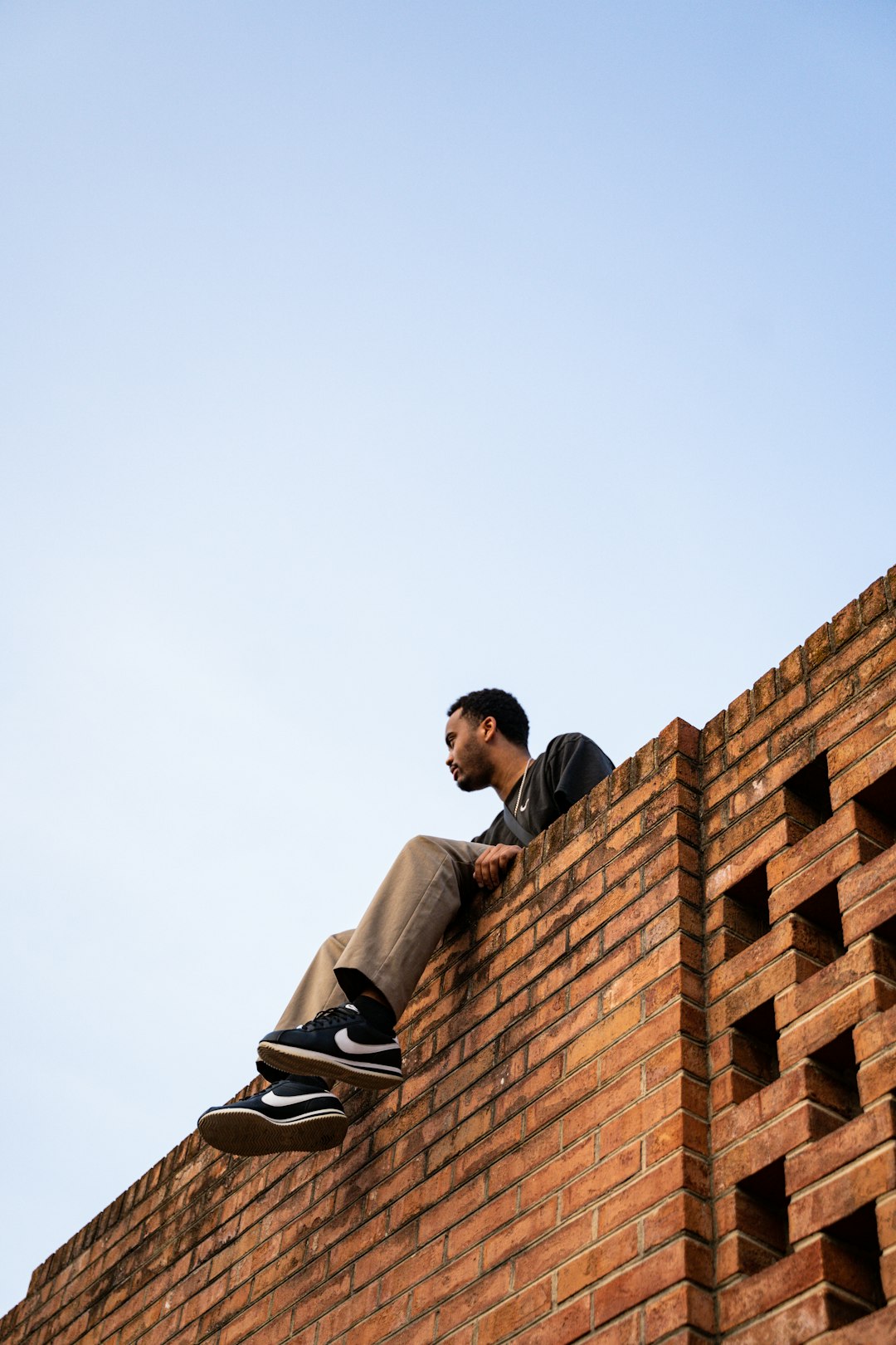 man in white long sleeve shirt sitting on brown concrete wall during daytime