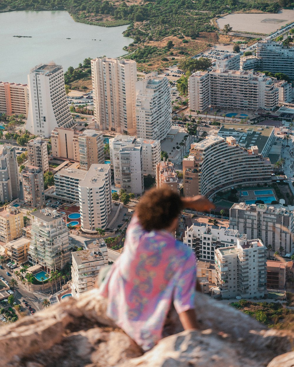woman in pink and white floral shirt sitting on top of building looking at city buildings