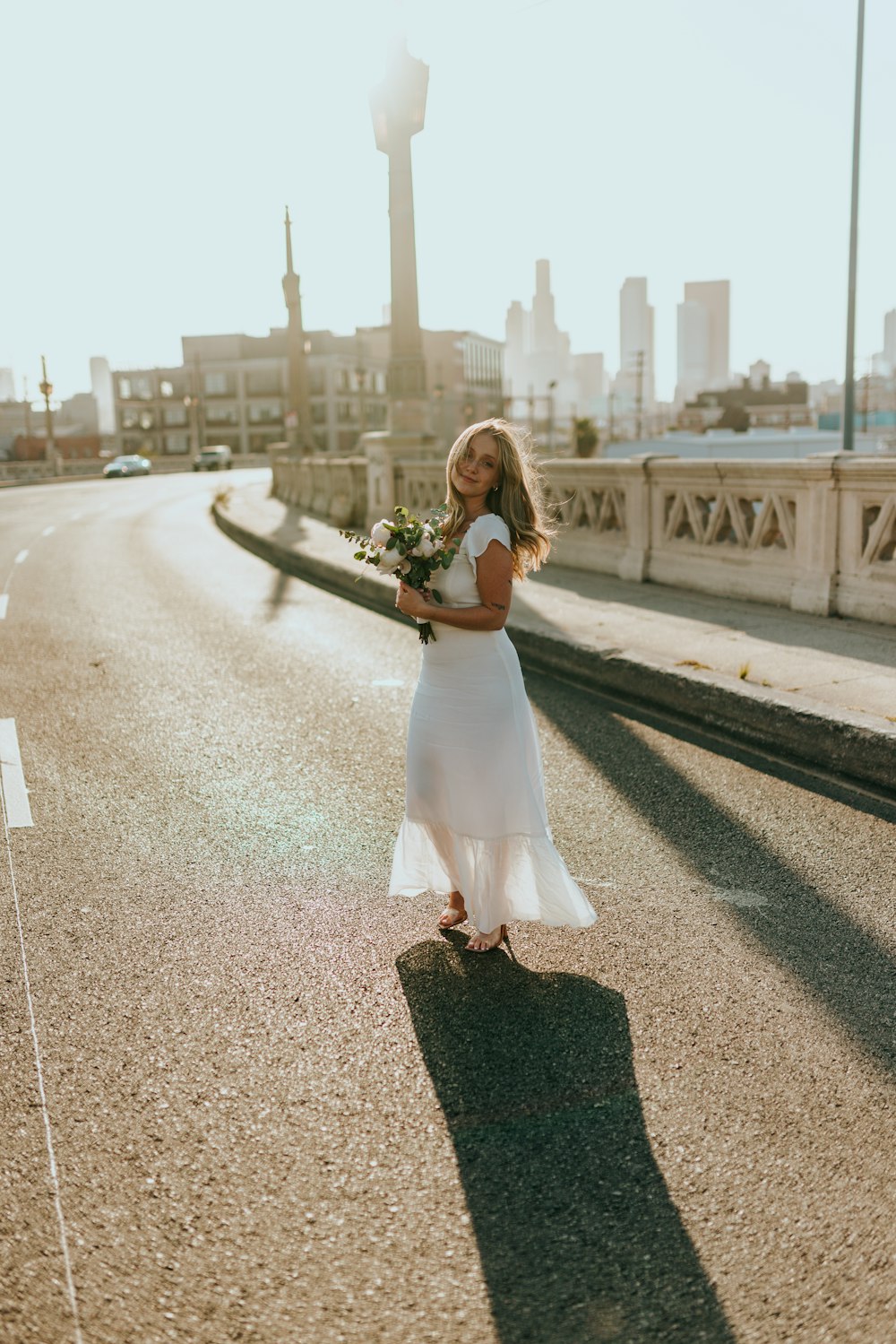 woman in white dress holding bouquet of flowers walking on sidewalk during daytime