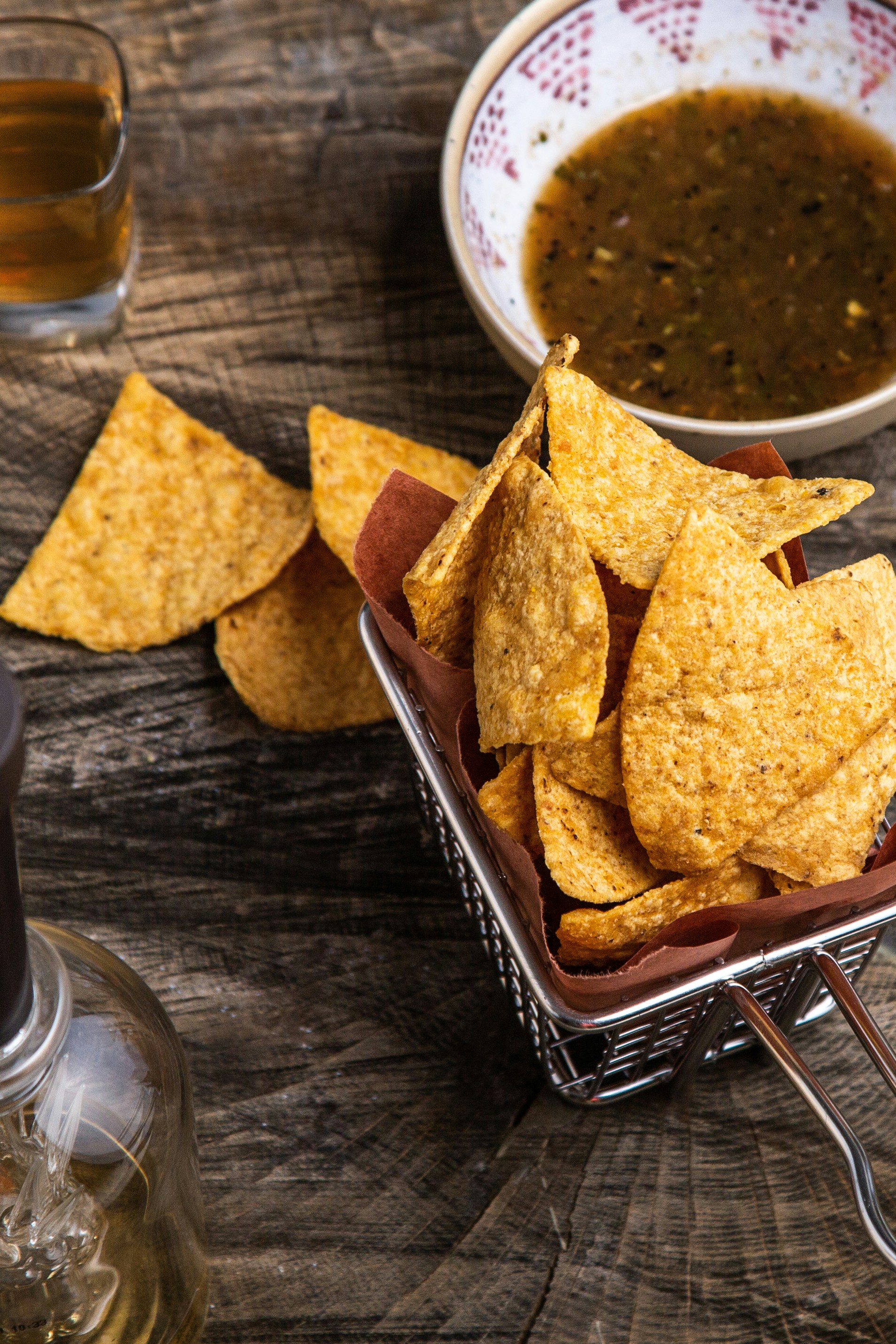 image of yellow corn tortilla chips in a yellow basket with a shot of tequila and a white bowl of red roasted salsa