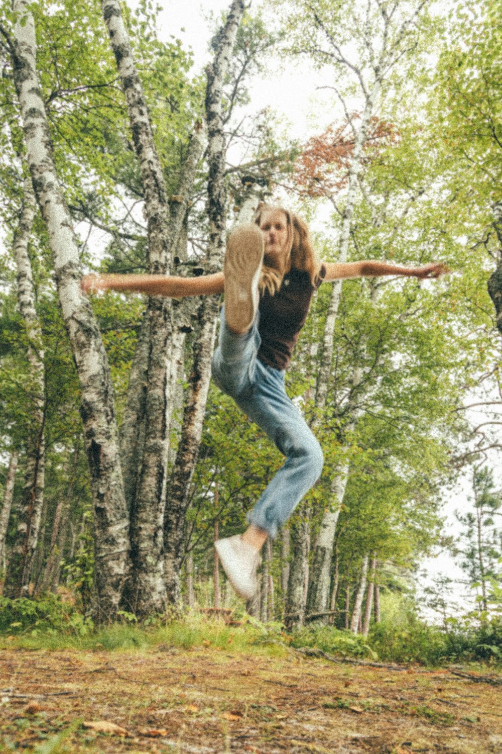 woman in black shirt and blue denim jeans jumping on brown tree branch during daytime