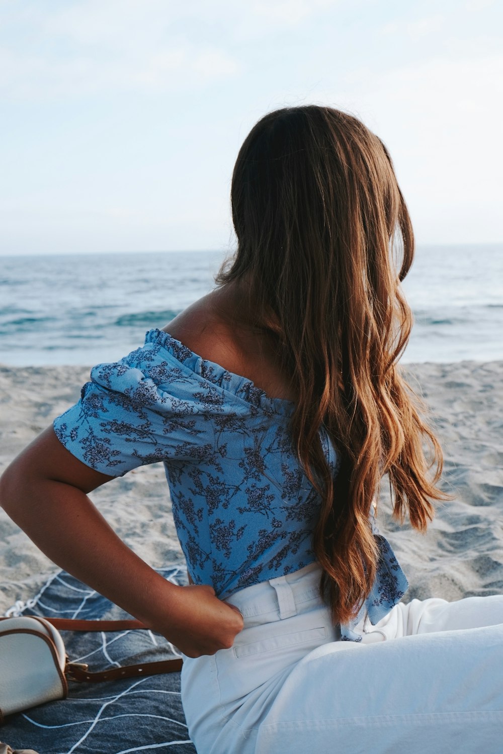 woman in white and blue floral dress sitting on white sand during daytime