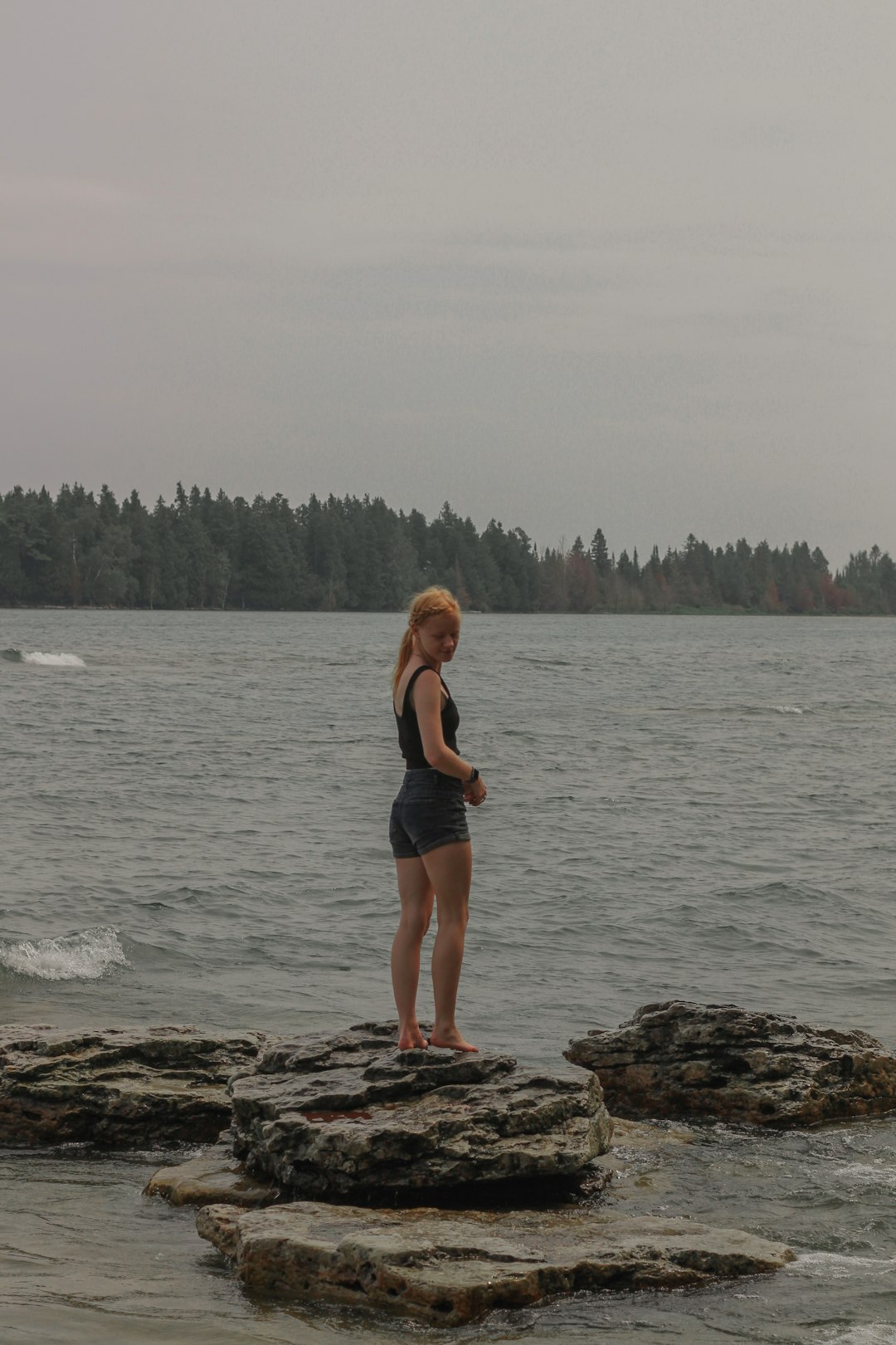 woman in black tank top and black shorts standing on rocky shore during daytime