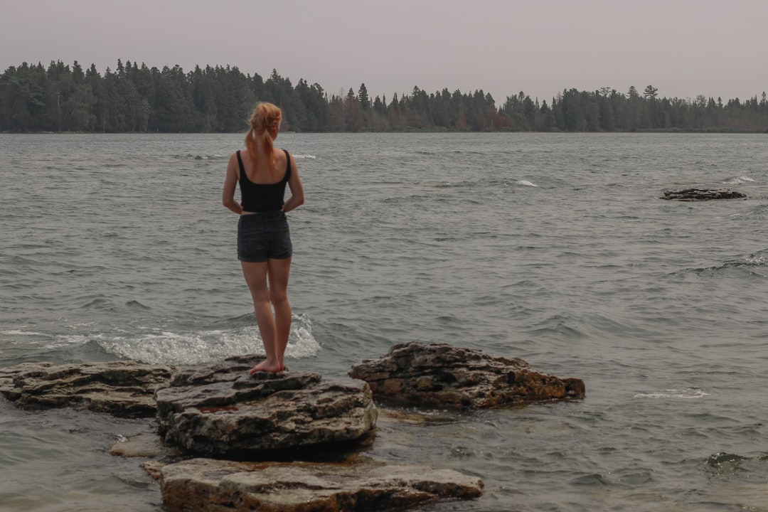 woman in black tank top and black shorts standing on brown rock in sea during daytime