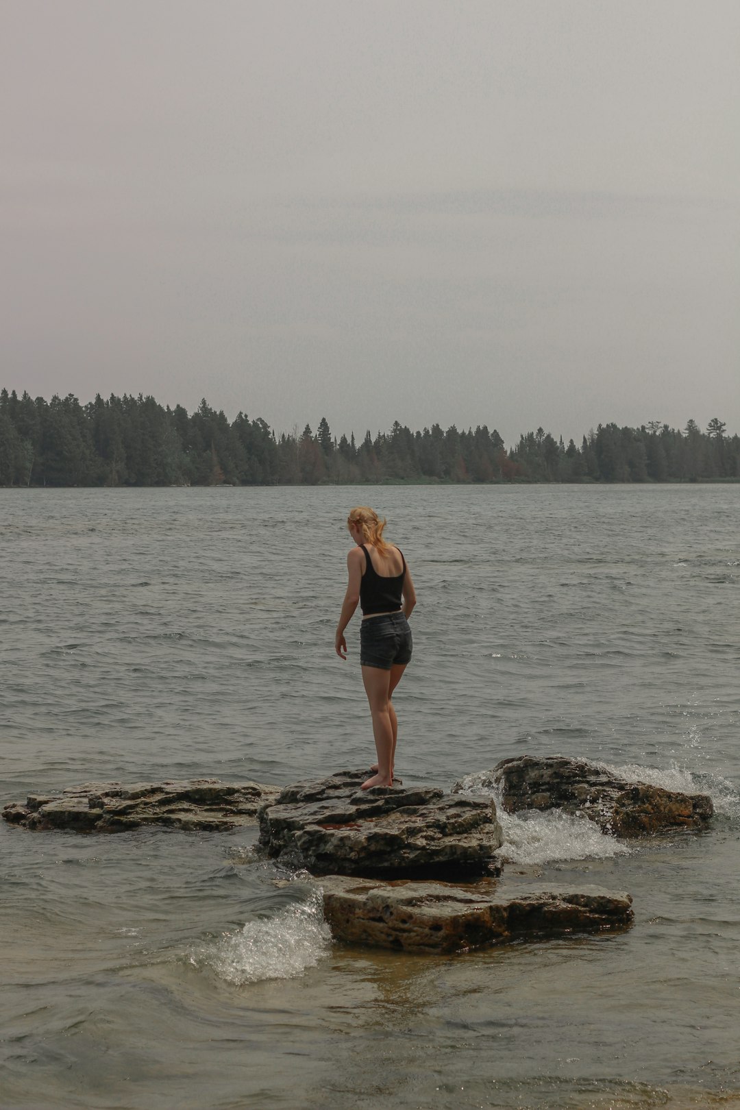 woman in black bikini standing on rock near body of water during daytime