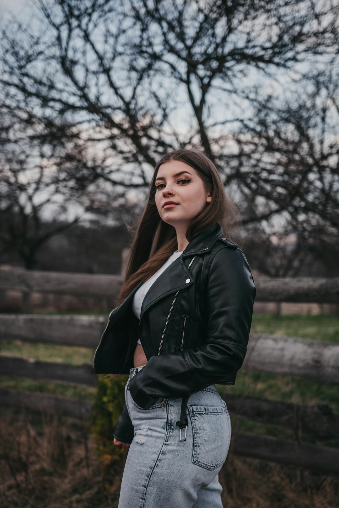 woman in black leather jacket standing near bare trees during daytime