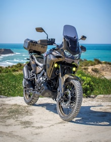 black and gray motorcycle on brown sand near body of water during daytime