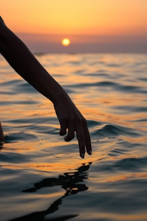 A diver gently touching the surface of a clear lagoon at sunset.