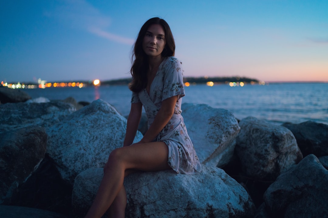 woman in white shirt and gray skirt sitting on gray rock near body of water during