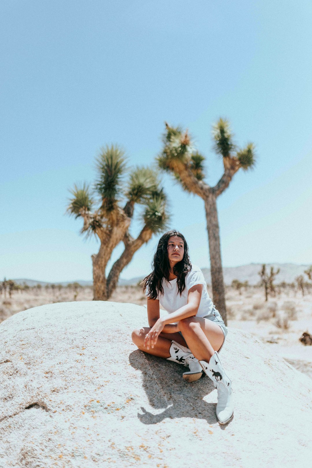 woman in white shirt sitting on brown rock during daytime