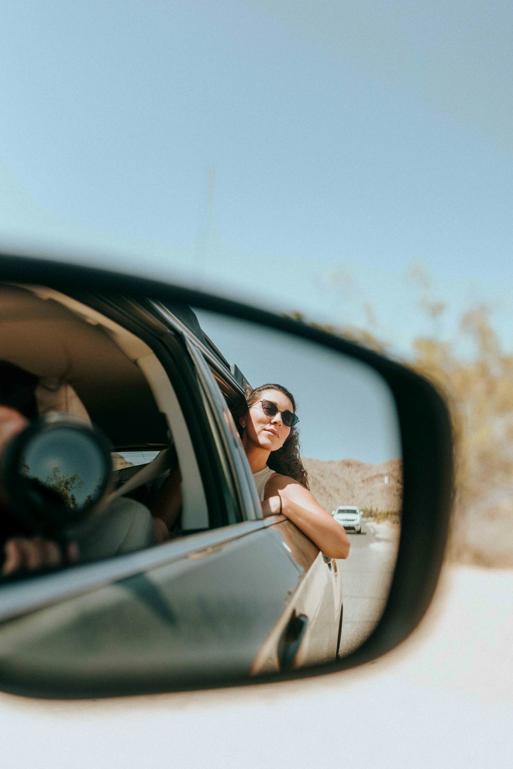 Frau in weißem Hemd und braunem Rock mit schwarzer Sonnenbrille fährt tagsüber Auto