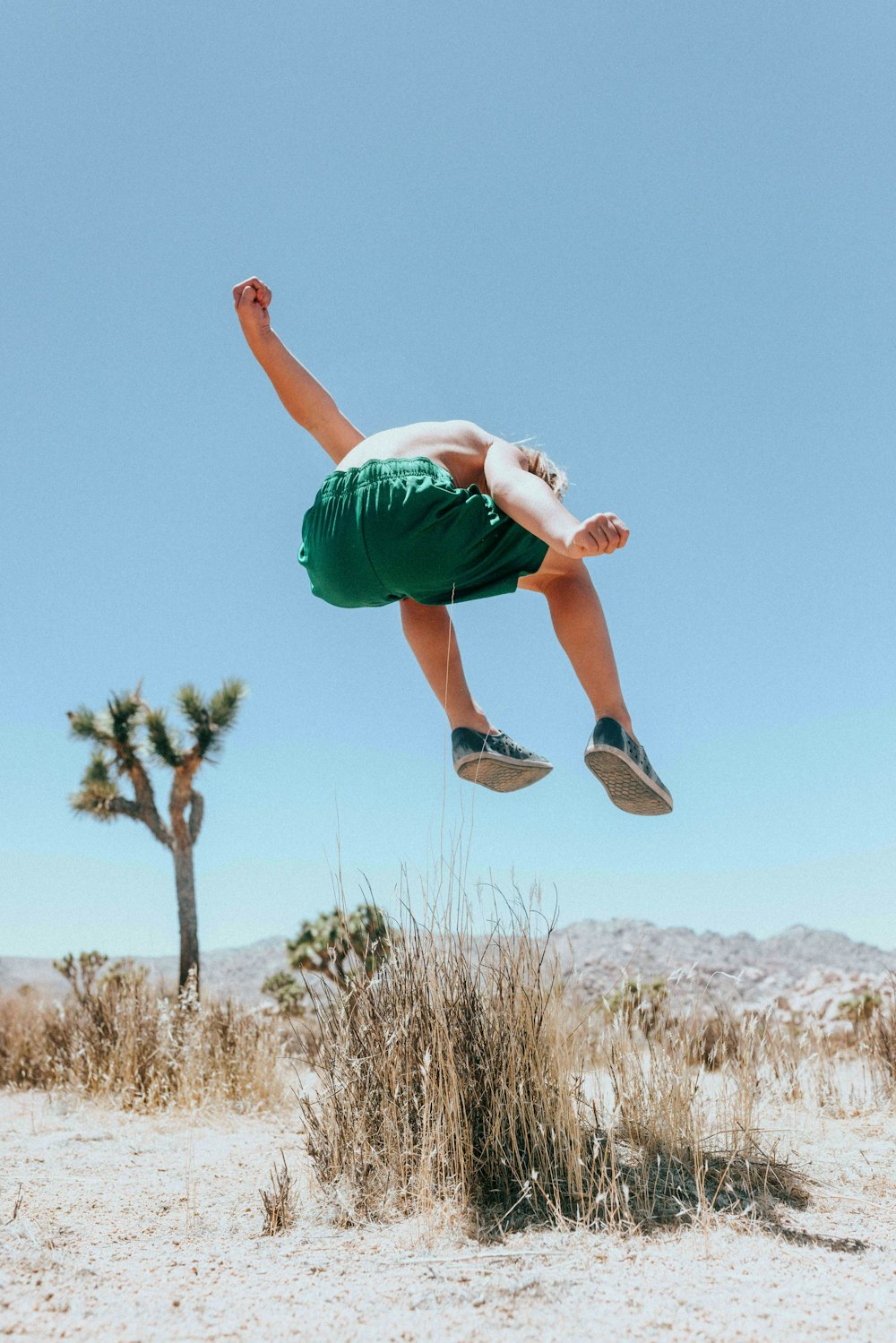 man in green t-shirt and green shorts jumping on brown grass field during daytime