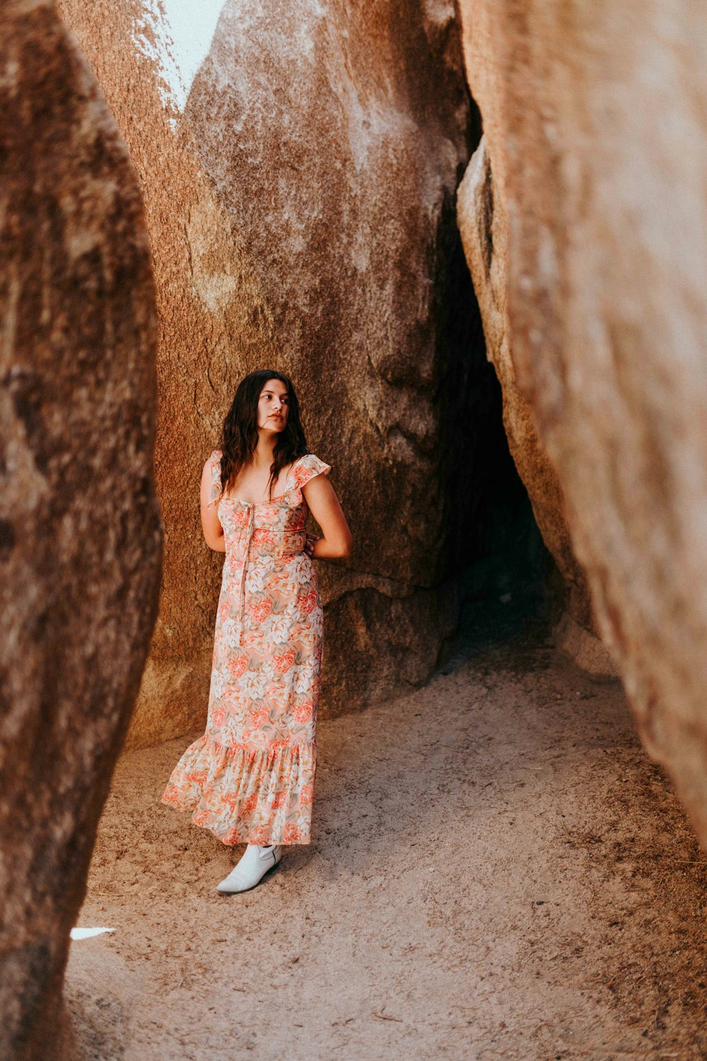 woman in white and pink floral dress leaning on brown rock