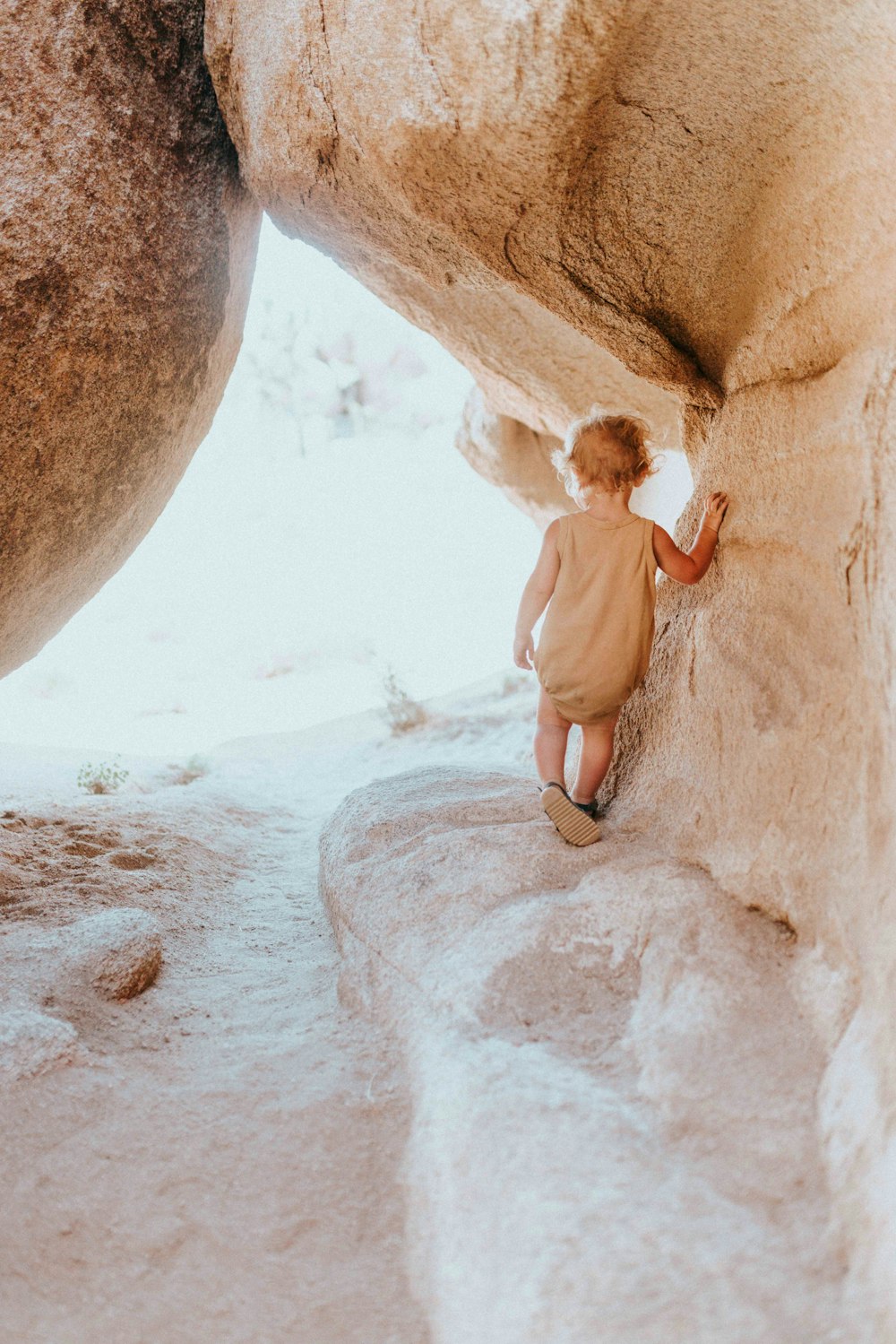 woman in white shirt and brown shorts climbing on brown rock