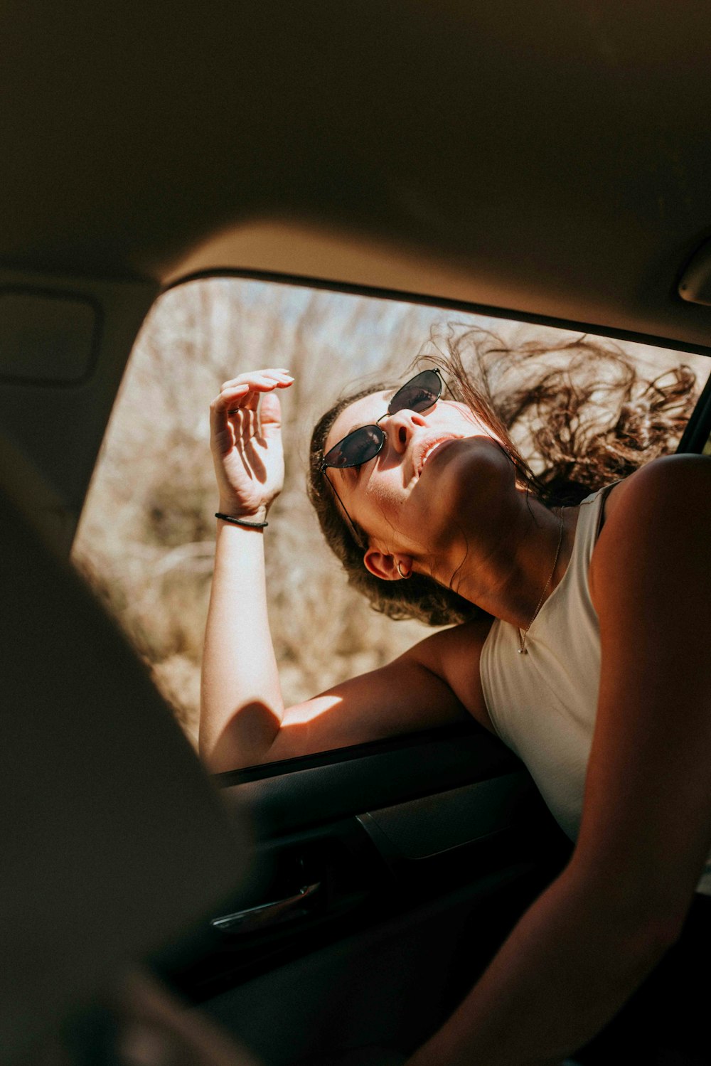 Mujer con camiseta blanca sin mangas con gafas de sol sentada dentro del coche