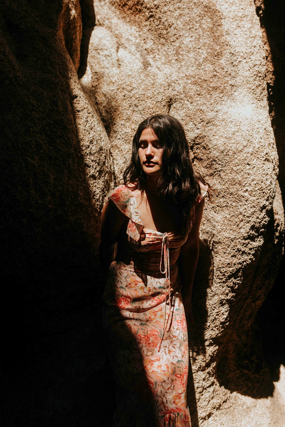 woman in black and white dress leaning on brown rock