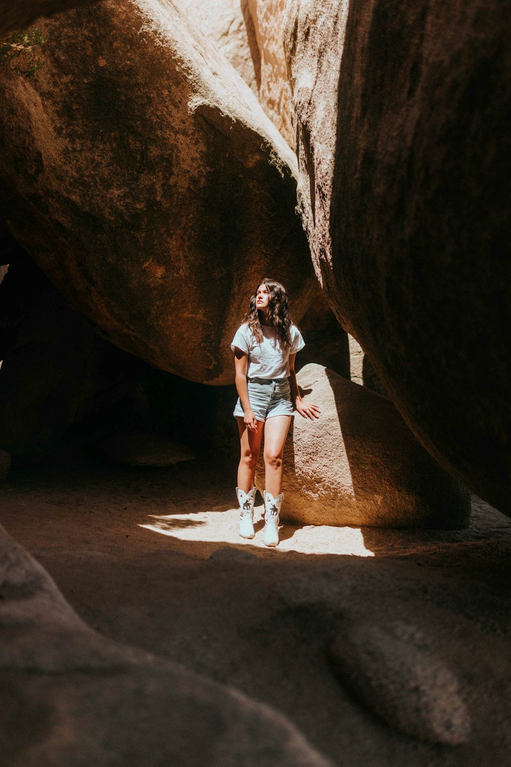 woman in white t-shirt and blue denim shorts standing in cave