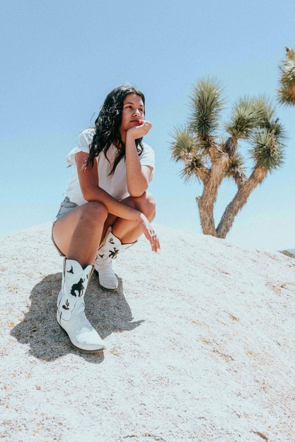 woman in white floral lace up boots sitting on white sand during daytime