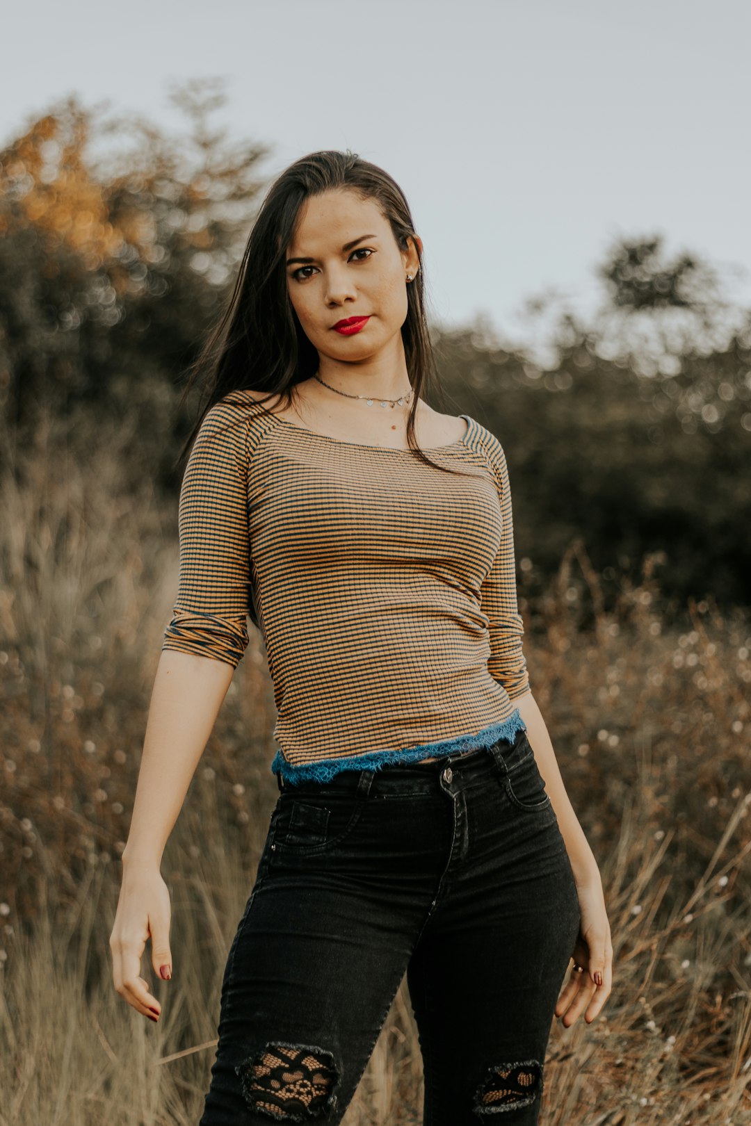 woman in brown long sleeve shirt and black denim jeans standing on grass field during daytime