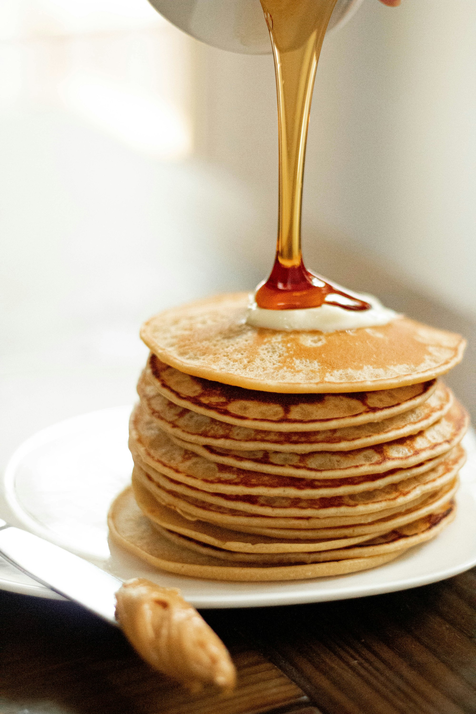 Syrup pouring over a tall stack of fluffy pancakes