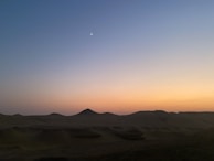 A peaceful desert scene at dusk with soft orange and rose pale hues blending into the horizon.